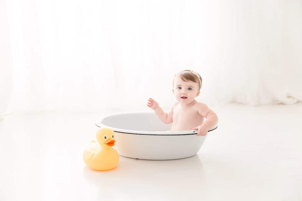 A baby plays in a tub with a yellow duckie. 