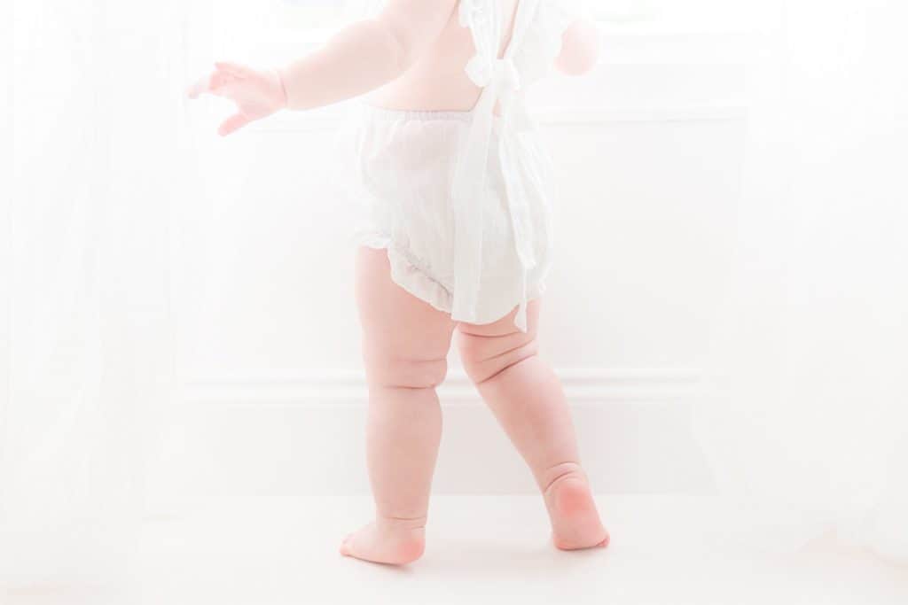 A baby's knee fat rolls up as she stands. 