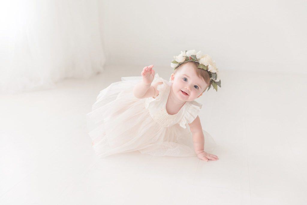 A baby crawls on the floor while wearing a flower crown during her First Birthday photoshoot