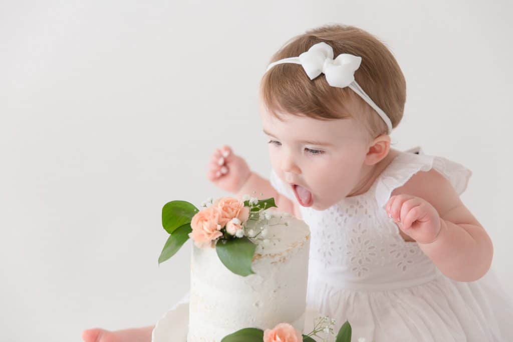 A baby girl licks her birthday cake. 