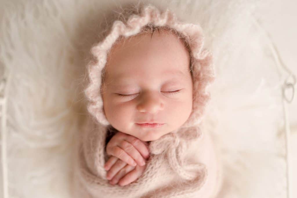 A small newborn sleeps with a knitted bonnet on her head. 