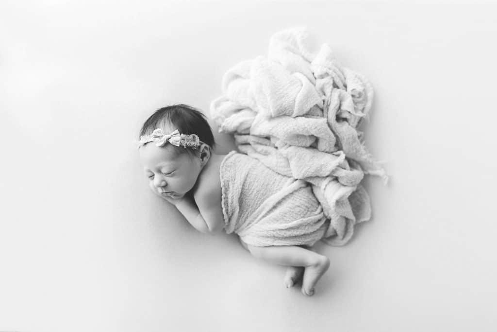 A newborn sleeps while wrapped in a flowing, white blanket. 