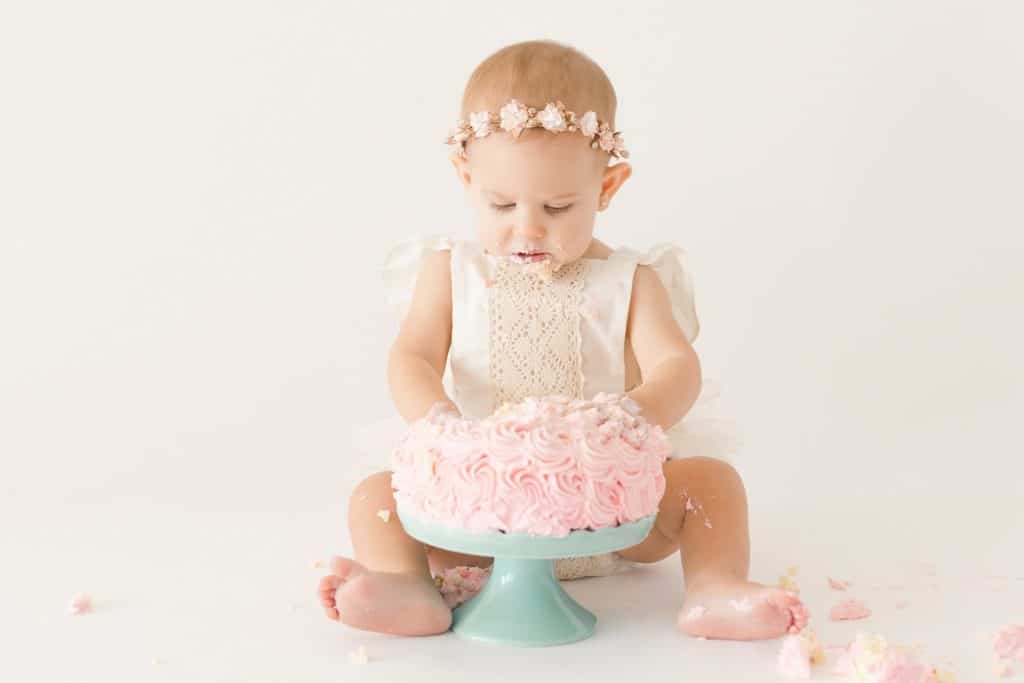 A baby girl squishes her fingers into her birthday cake.