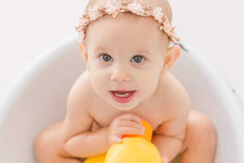 A baby girl plays with a yellow rubber duck in an old bath tub.