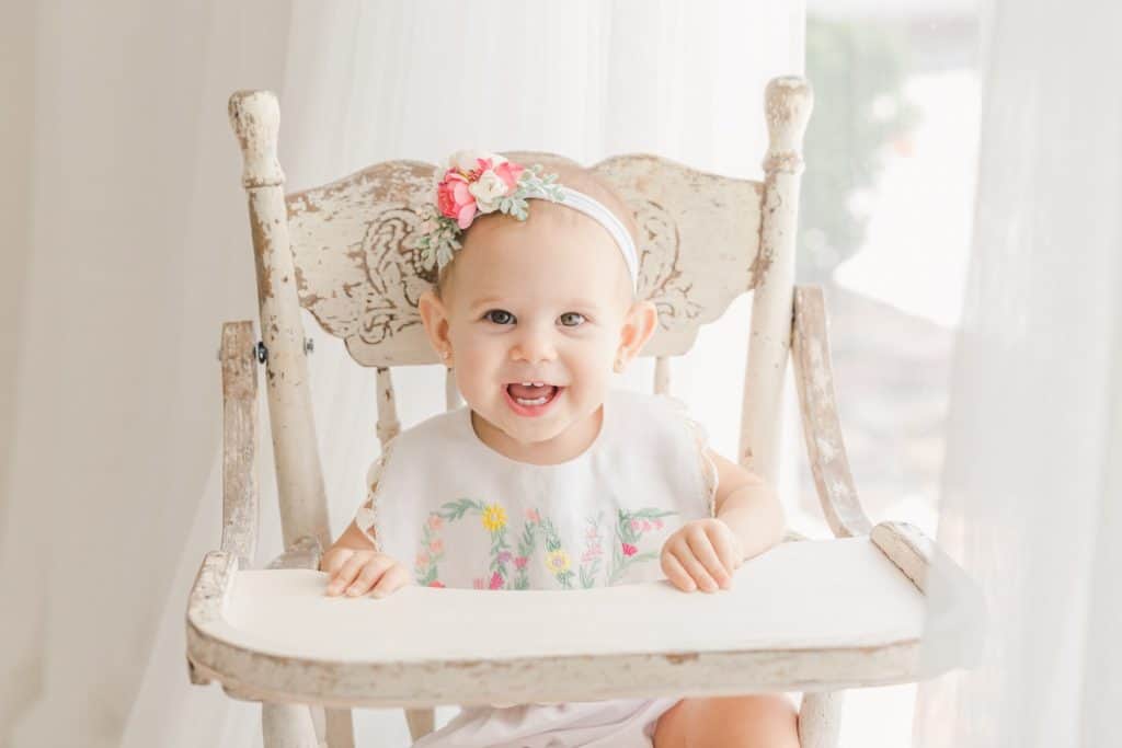 A baby girl sits in an antique high chair.