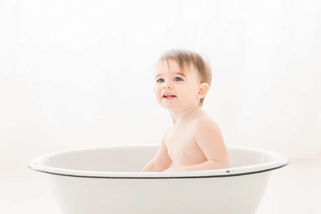 A baby girl sits in an antique bath tub to play. 