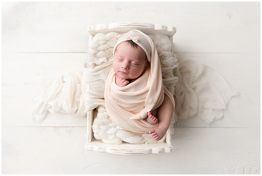  baby sleeping in a cradle prop swaddled in peach wrap