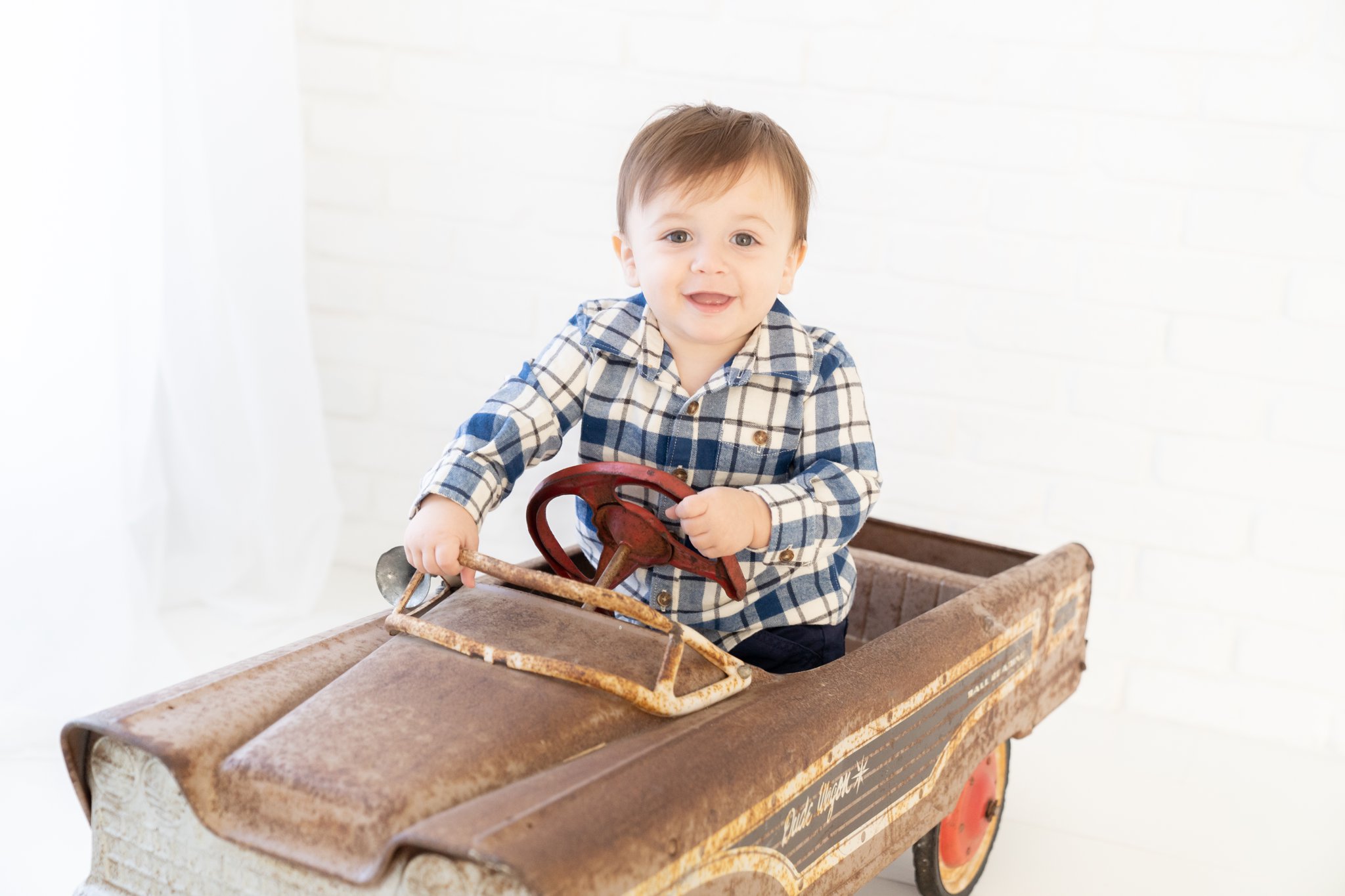 Baby boy being photographed in antique car in Jupiter Baby Photography studio.