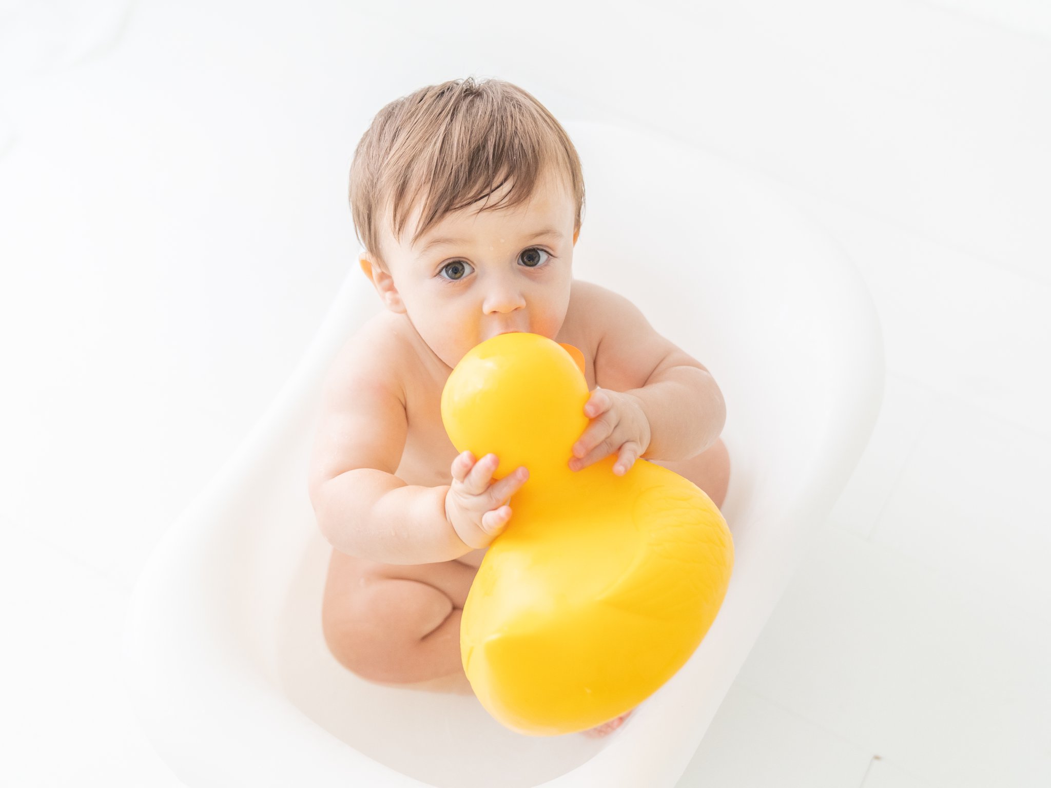 Baby boy splashing in water play tub while being photographed in Jupiter baby photography studio.