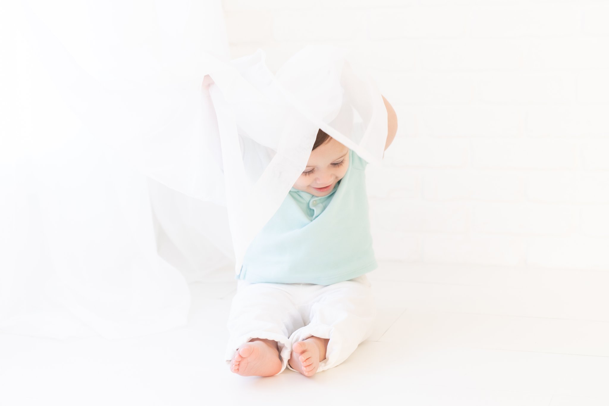 Baby boy playing in white curtains in Jupiter Baby Photography studio.