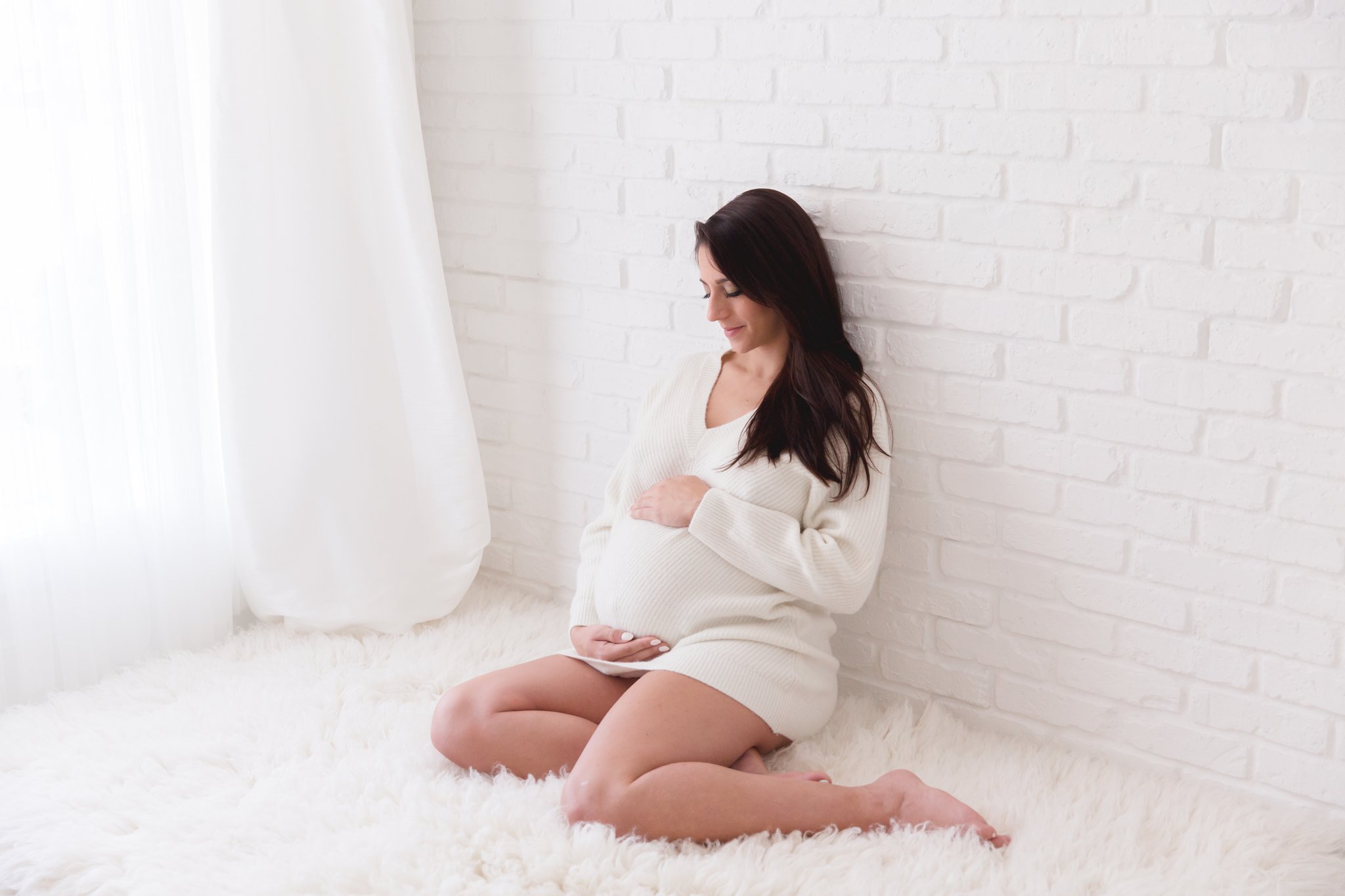 close up of baby bump of expecting mom resting on furry cream rug leaning against wall