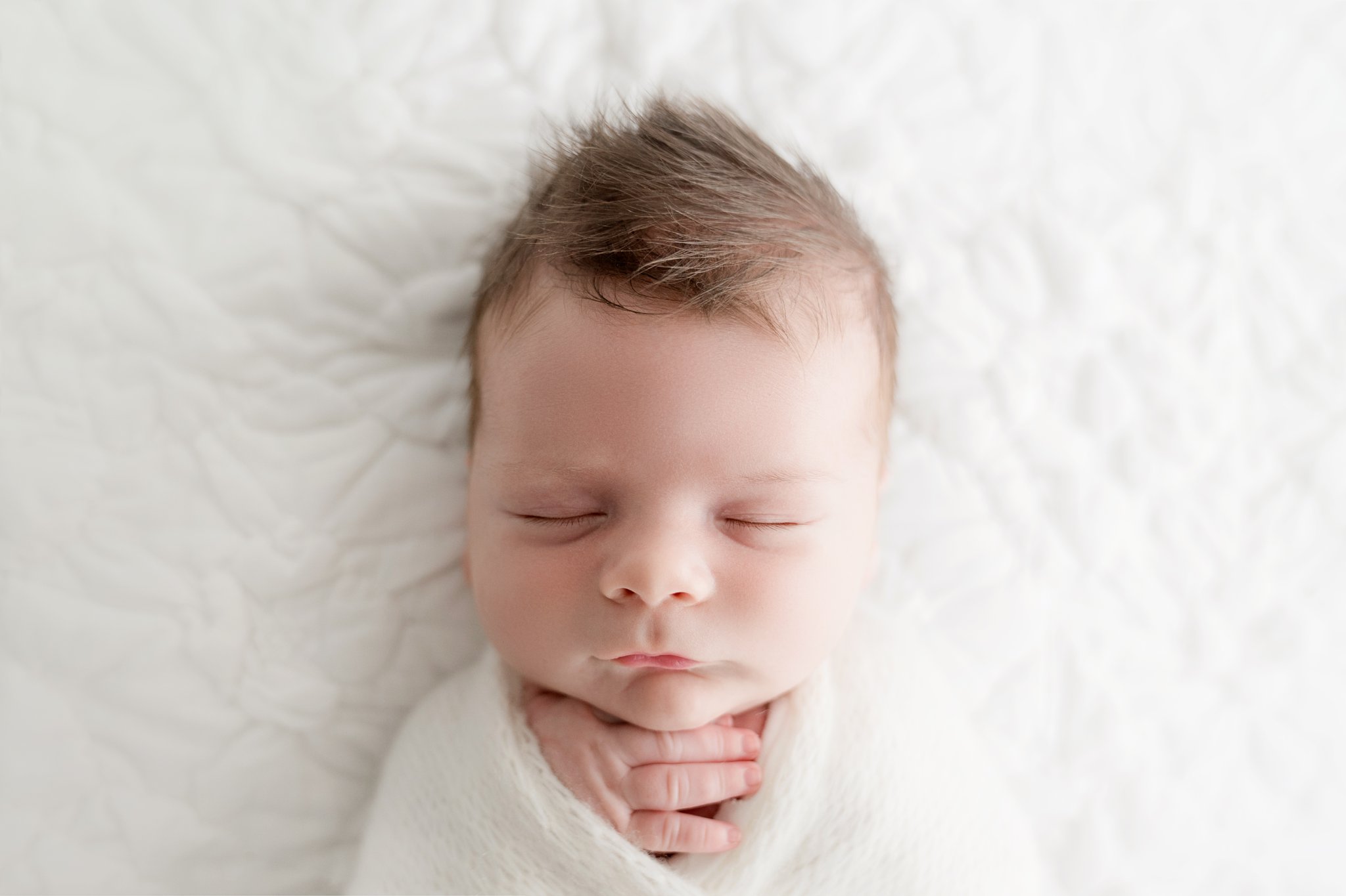 Photo of newborn baby boy being photographed in Jupiter Florida photography studio wrapped in a cream swaddle