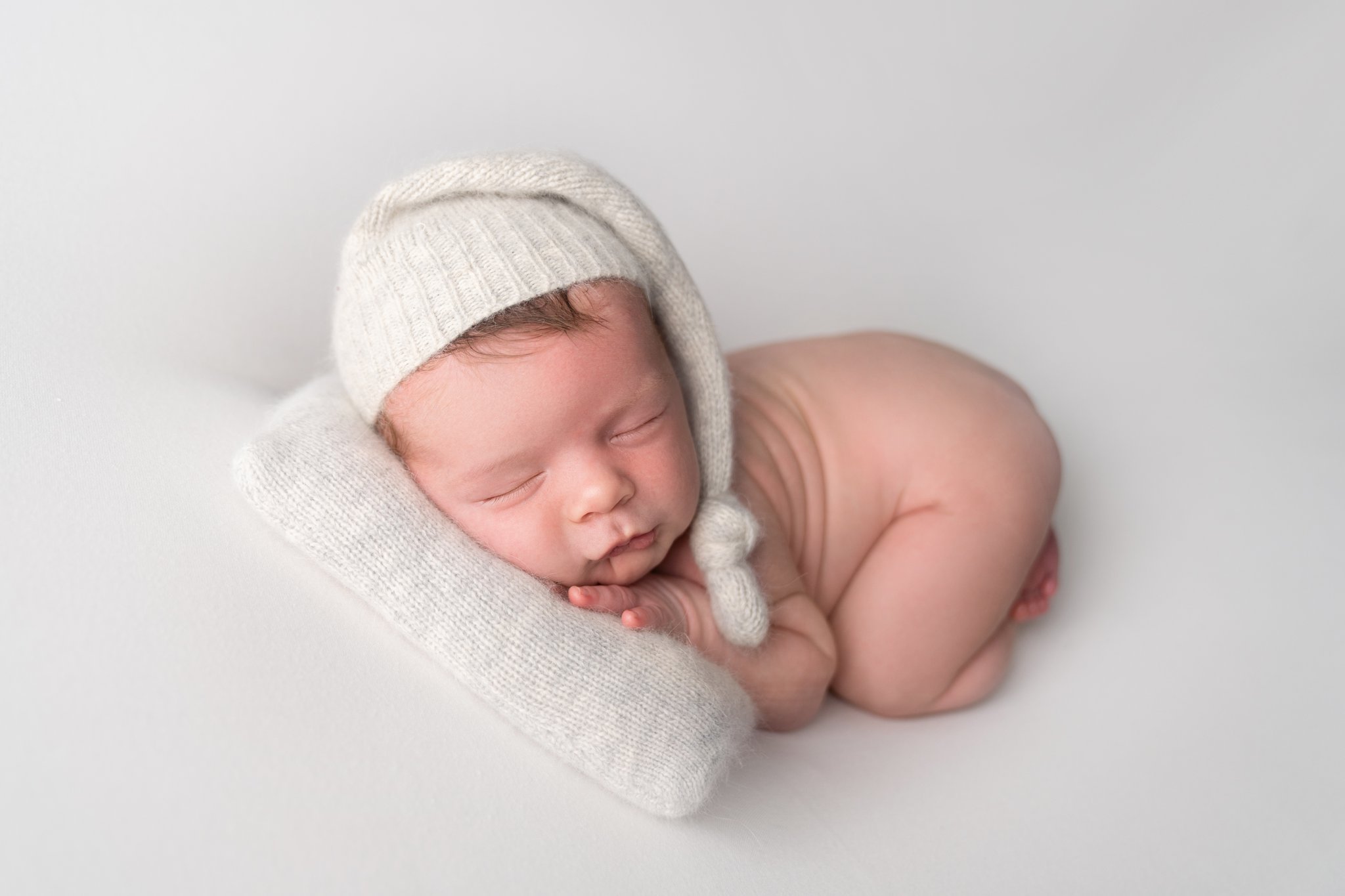 Photo of newborn baby boy being photographed in Jupiter Florida photography studio on cream backdrop with cream sleep cap and cream pillow