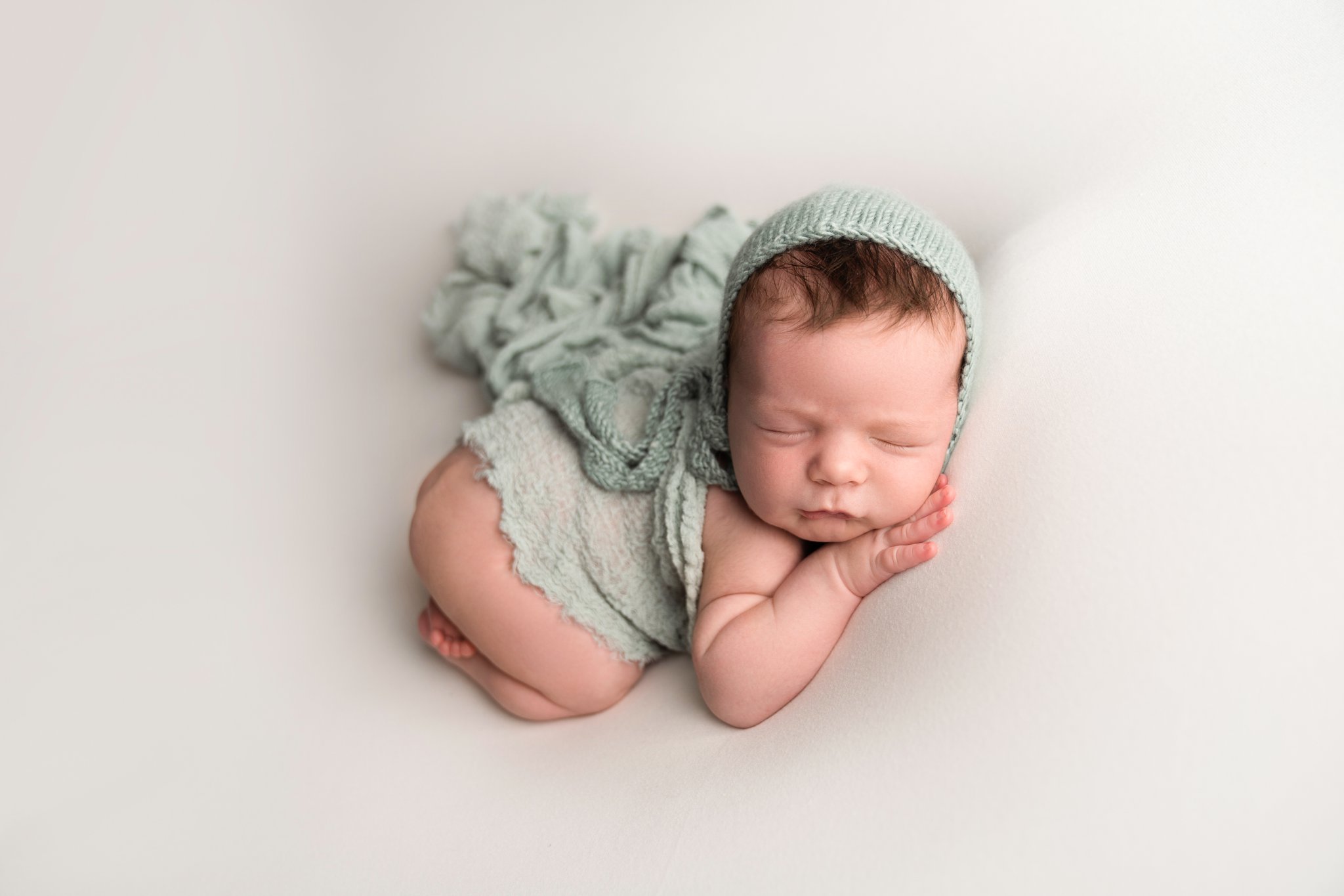 portrait of newborn baby boy being photographed in Jupiter Florida photography studio on cream backdrop with blue scarf draped over his back and a blue matching knitted bonnet 