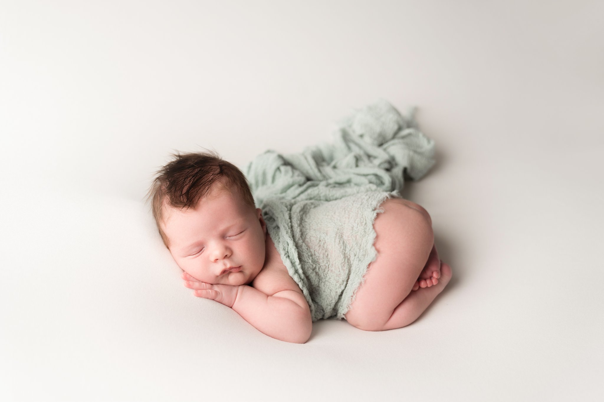 portrait of newborn baby boy being photographed in Jupiter Florida photography studio on cream backdrop with blue scarf draped over his back