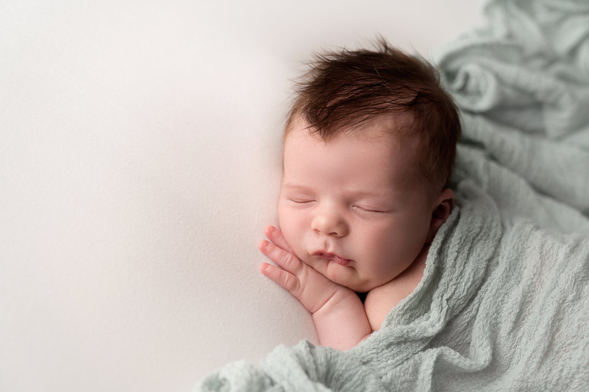 close-up of newborn baby boy being photographed in Jupiter Florida photography studio on cream backdrop with blue scarf draped over his back