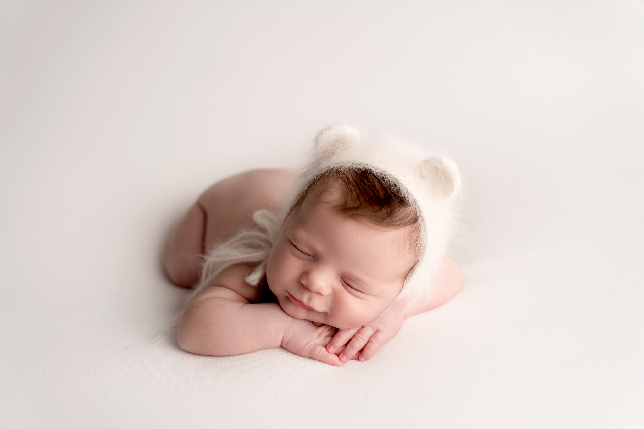 Newborn baby boy being photographed in Jupiter Florida photography studio wearing little bear hat on cream backdrop
