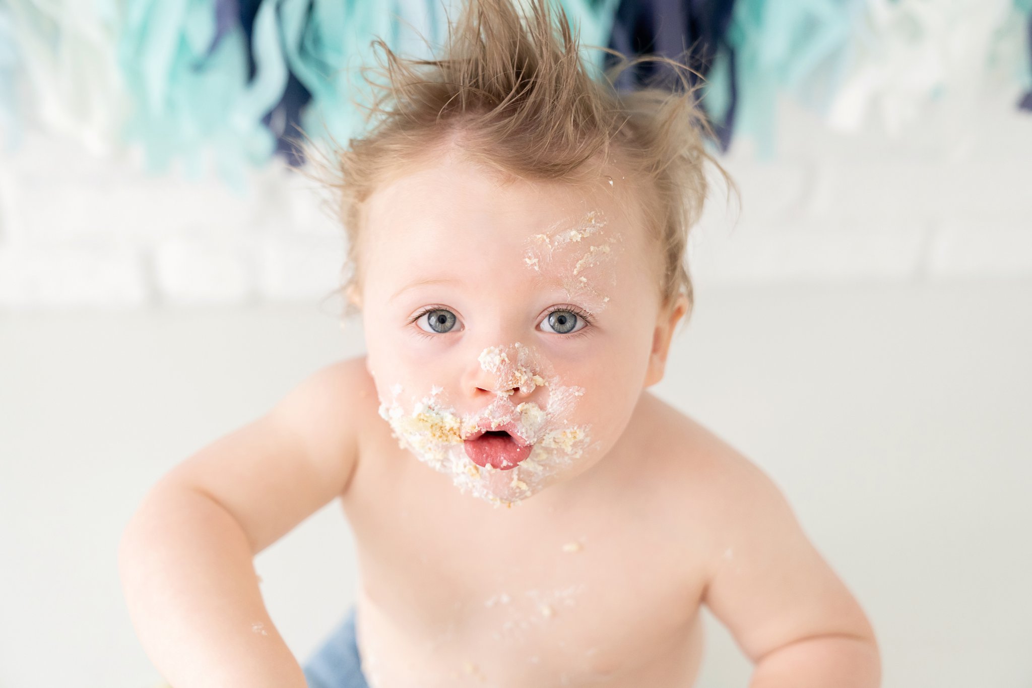 One year old baby in jeans eating and smashing his birthday cake in south florida baby photography studio. 