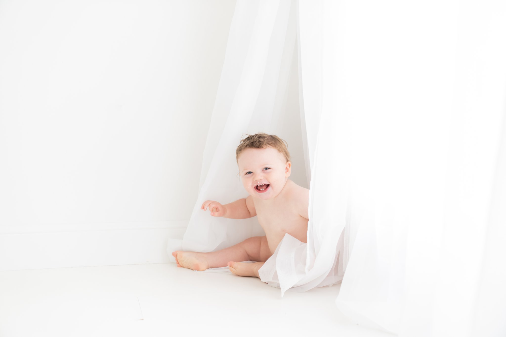 One year old baby iplaying in white sheer curtains in south florida baby photography studio. 