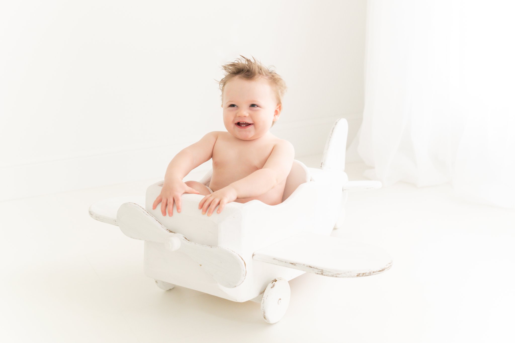 One year old baby in a white airplane prop. 