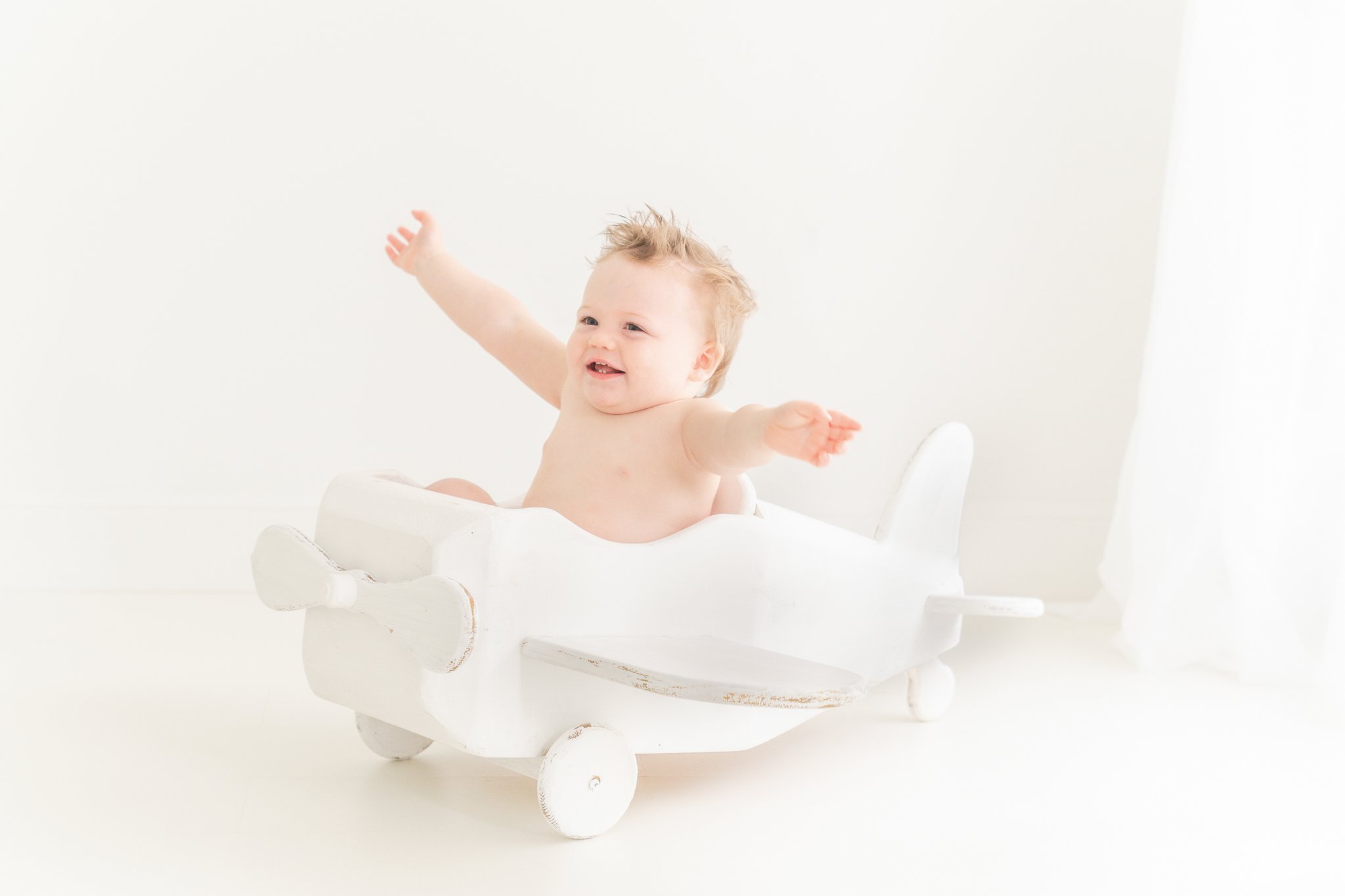 One year old baby in a white airplane prop. 