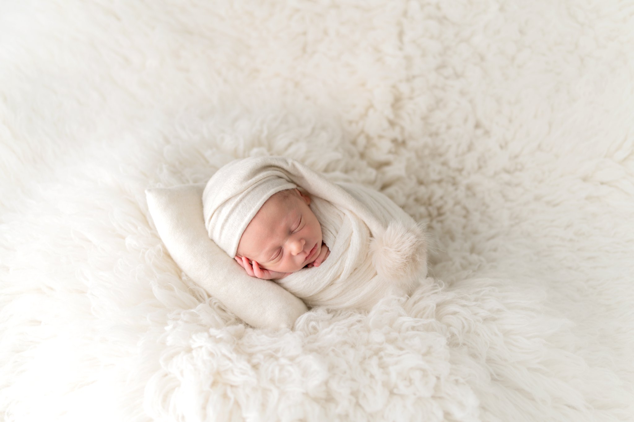 Newborn baby in off white swaddle, sleepy hat and pillow being photographed in south florida photo studio.