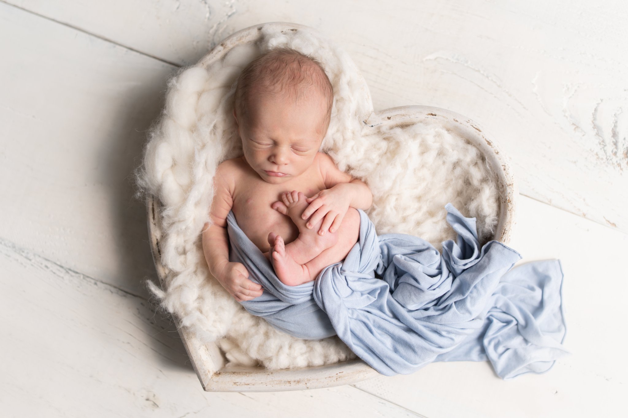 Newborn baby laying in heart shaped posing prop being photographed inJupiter photo studio.