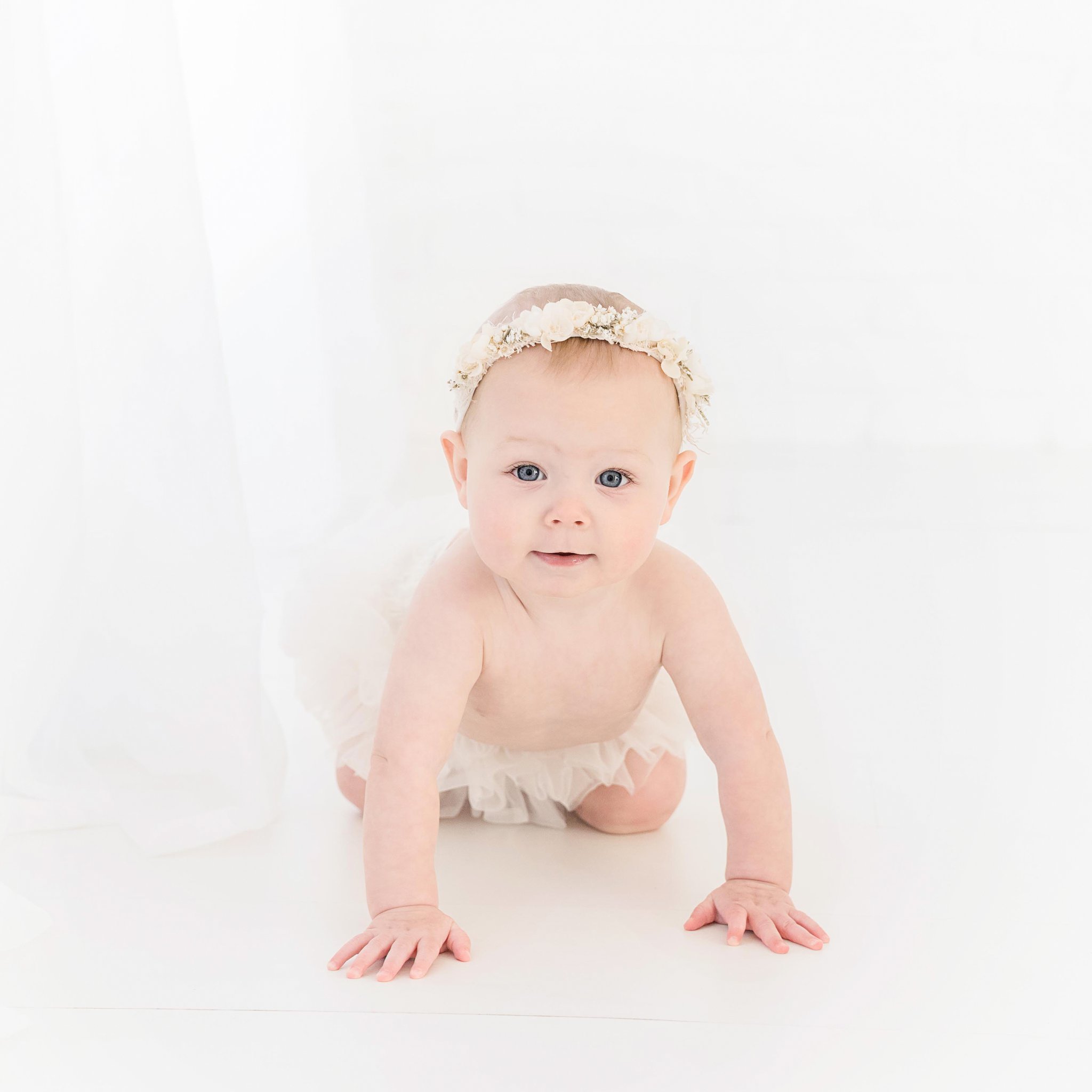 Sitter 6-7 month old baby with flower halo on her head being photographed in Jupiter photography studio
