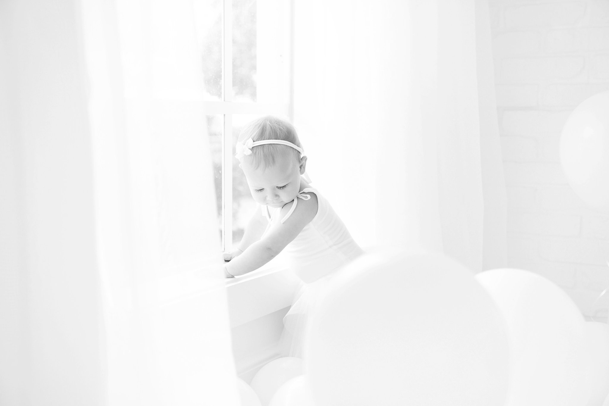 Birthday baby girl being photographed in a south florida photography studio filled with white balloons.