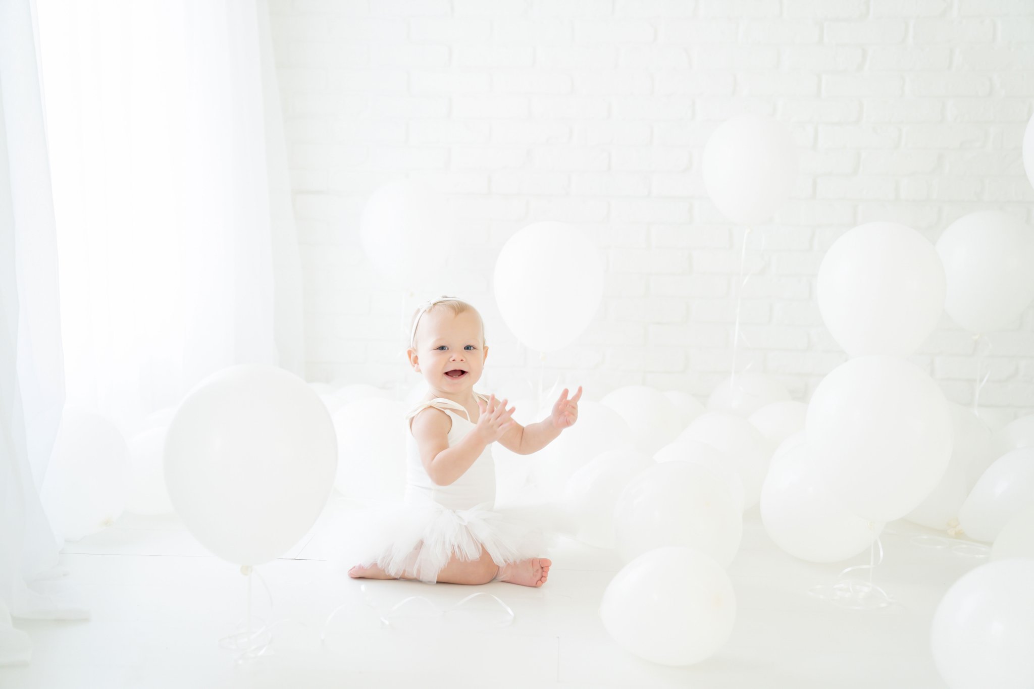 Birthday baby girl being photographed in a south florida photography studio filled with white balloons.