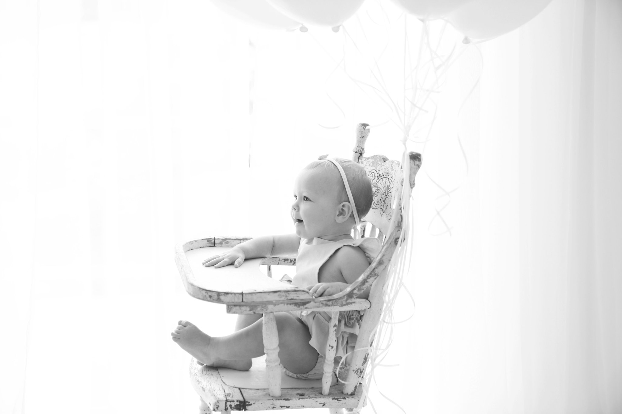 Birthday baby girl being photographed in a south florida photography studio in blue ruffled romper in an antique high chair with a huge bouquet of balloons.