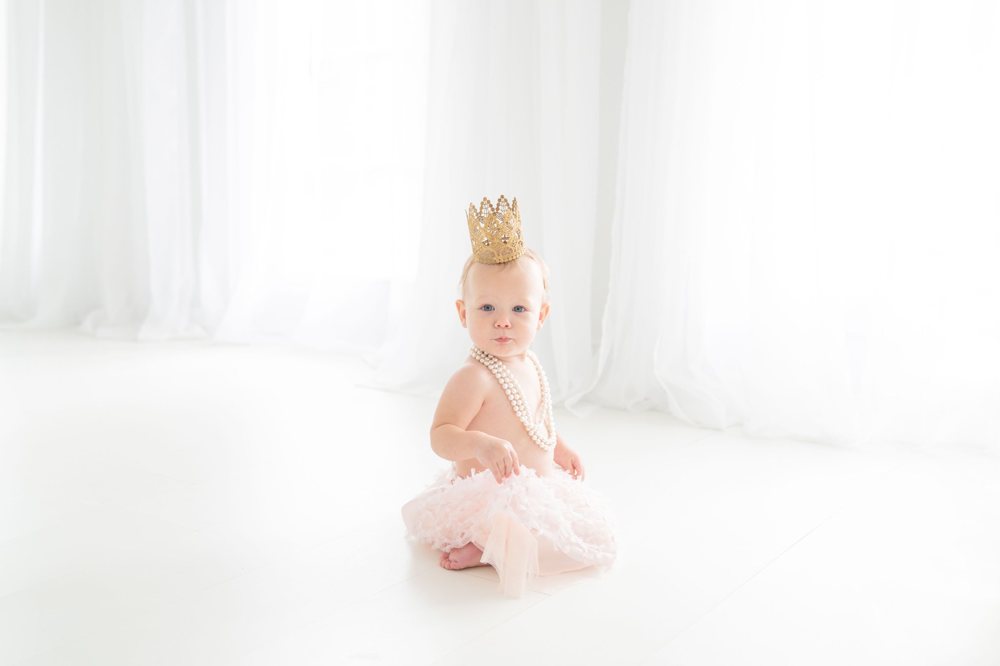 Baby girl being photographed in a Jupiter florida photography studio in a Chanel style blush pink skirt and princess crown