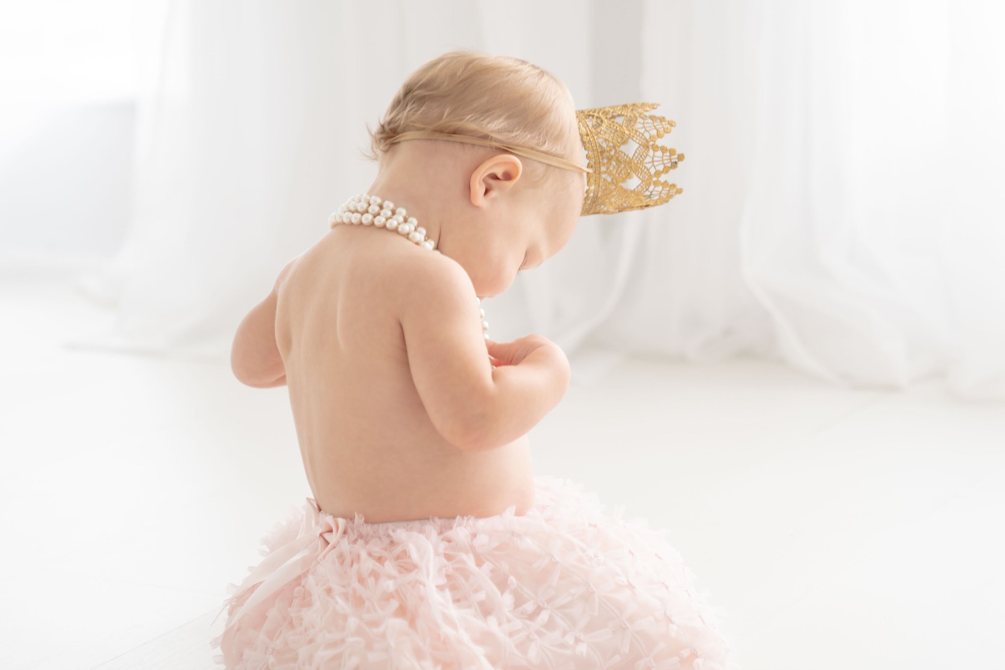 Baby girl being photographed in a Jupiter florida photography studio in a Chanel style blush pink skirt and princess crown