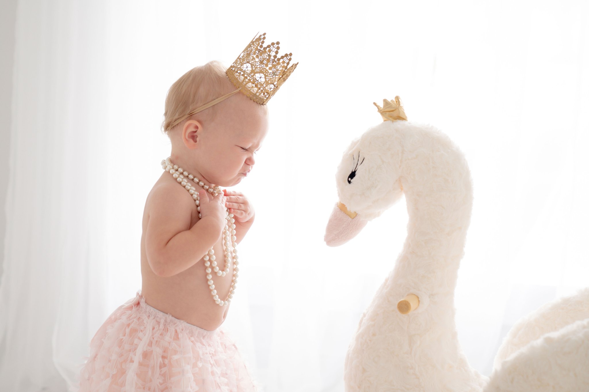 One Year old being photographed in a Jupiter Florida photography studio wearing pink skirt and crown and standing by a rocking swan.