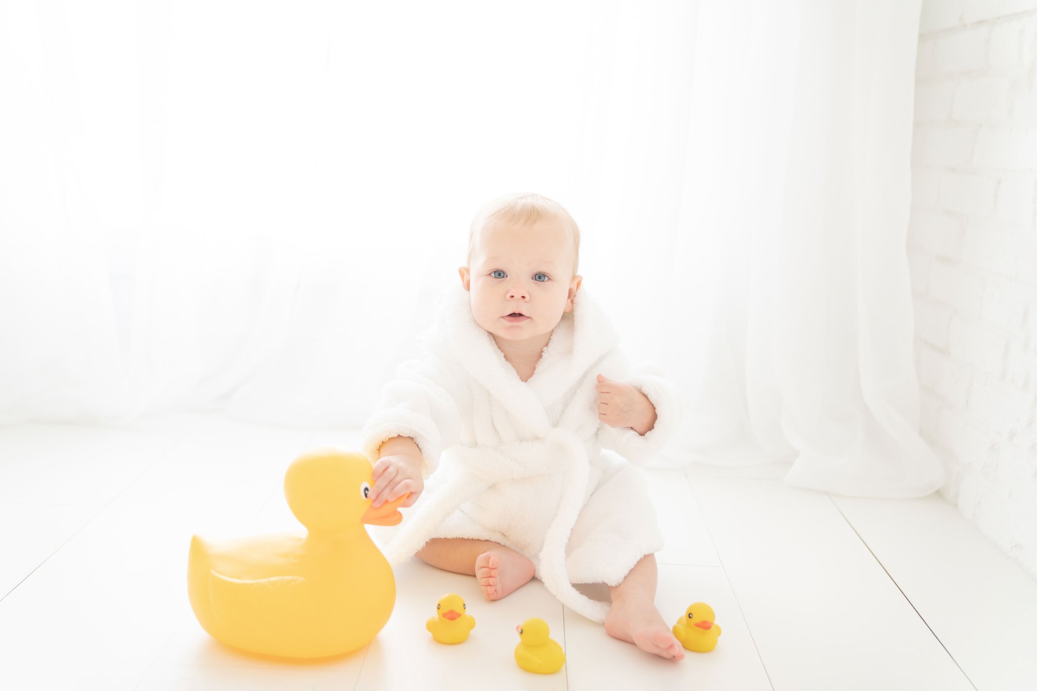 One Year old being photographed in a Jupiter Florida photography studio playing in a claw foot white tub playing with rubber duckies