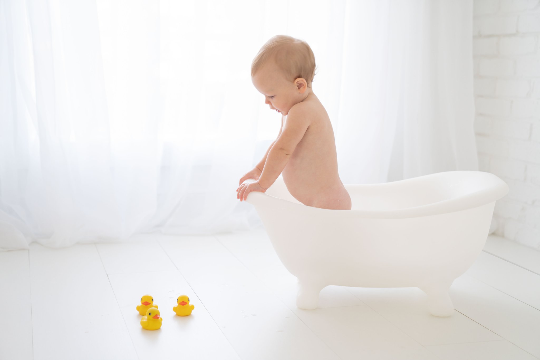 One Year old being photographed in a Jupiter Florida photography studio playing in a claw foot white tub playing with rubber duckies