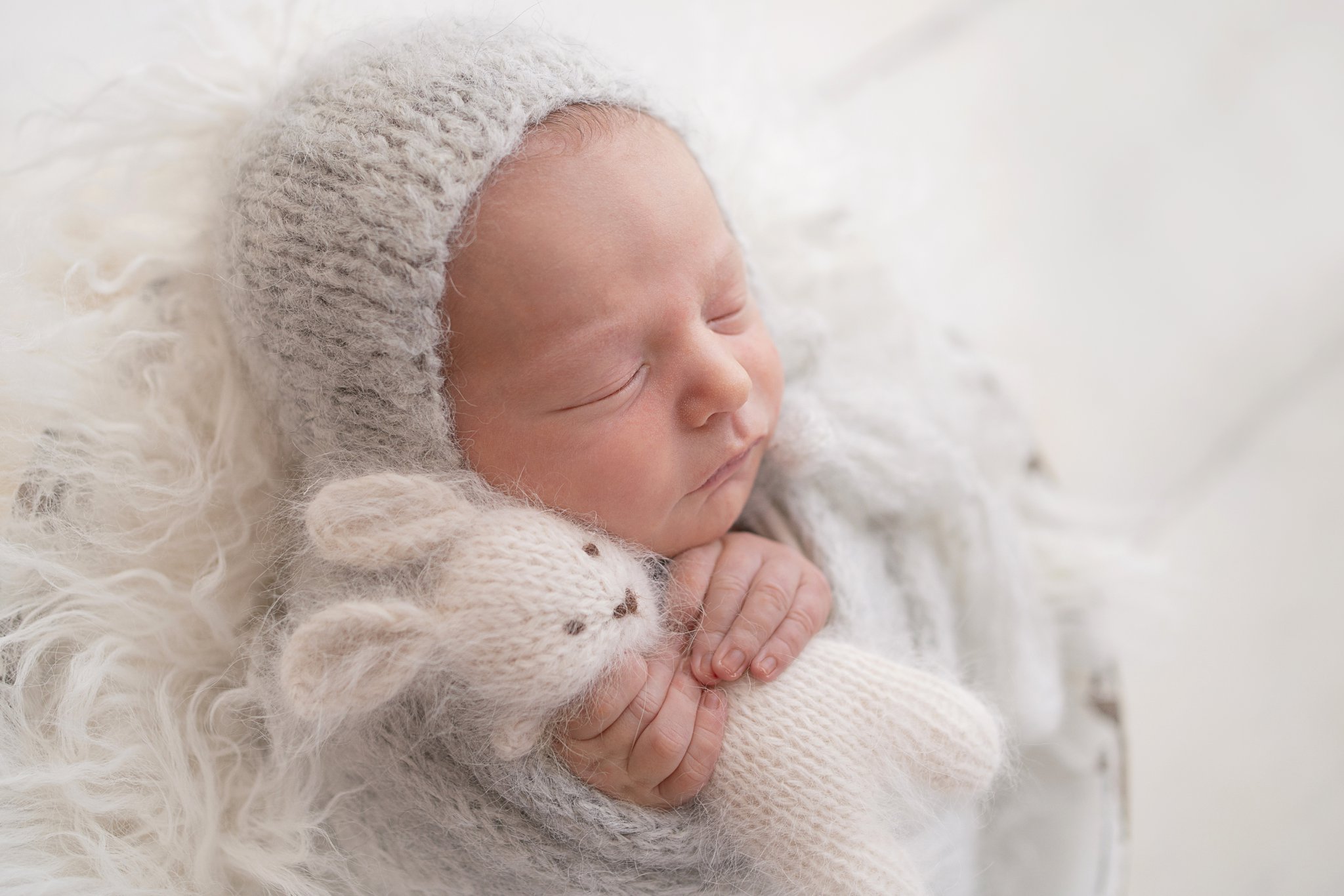 10 day old newborn posing in a wooden antique bucket holding a white stuffed bunny in jupiter florida photography studio