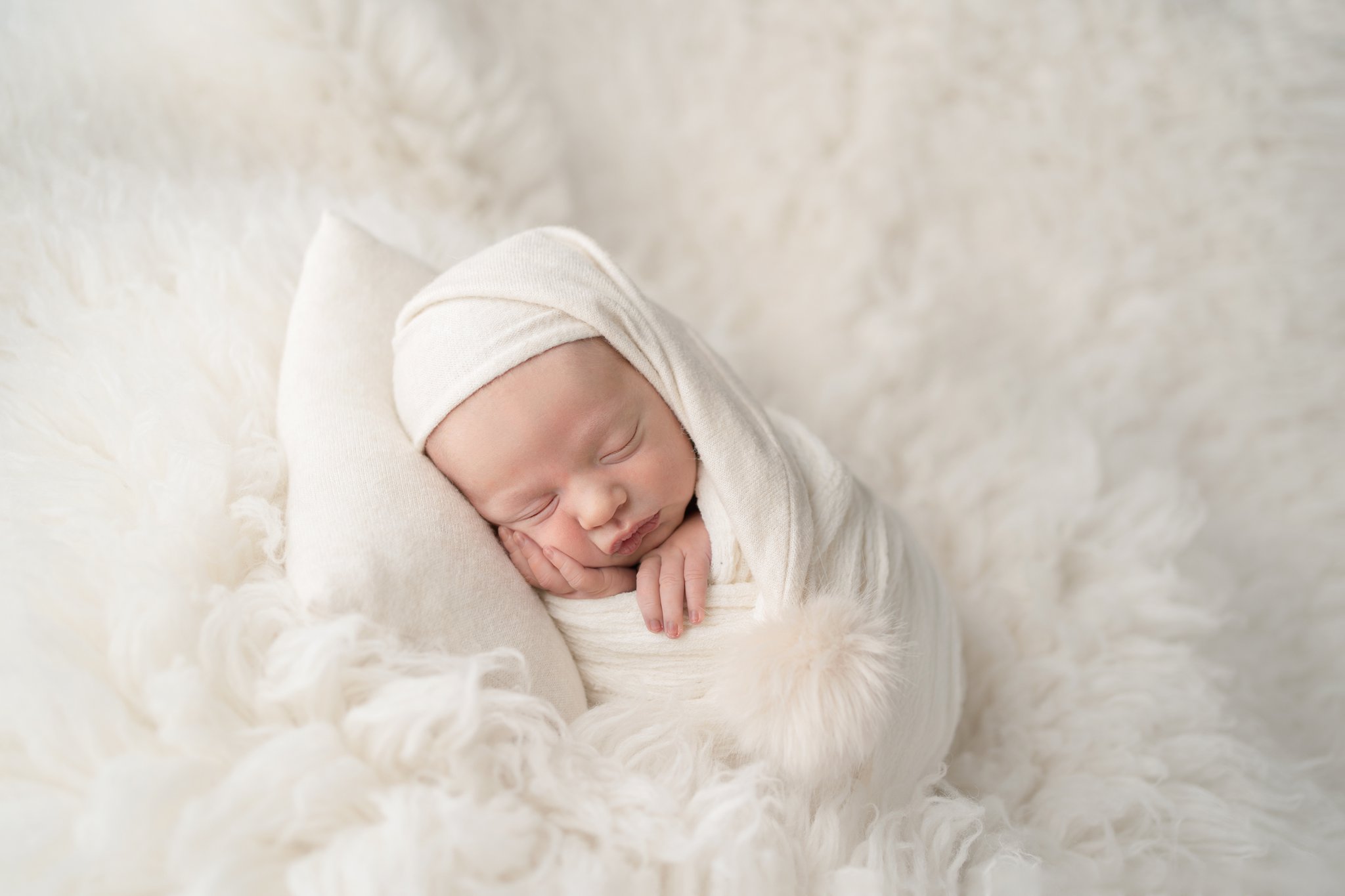 10 day old newborn posing on a white backdrop with a lsleepy cap all swaddled in jupiter florida photography studio
