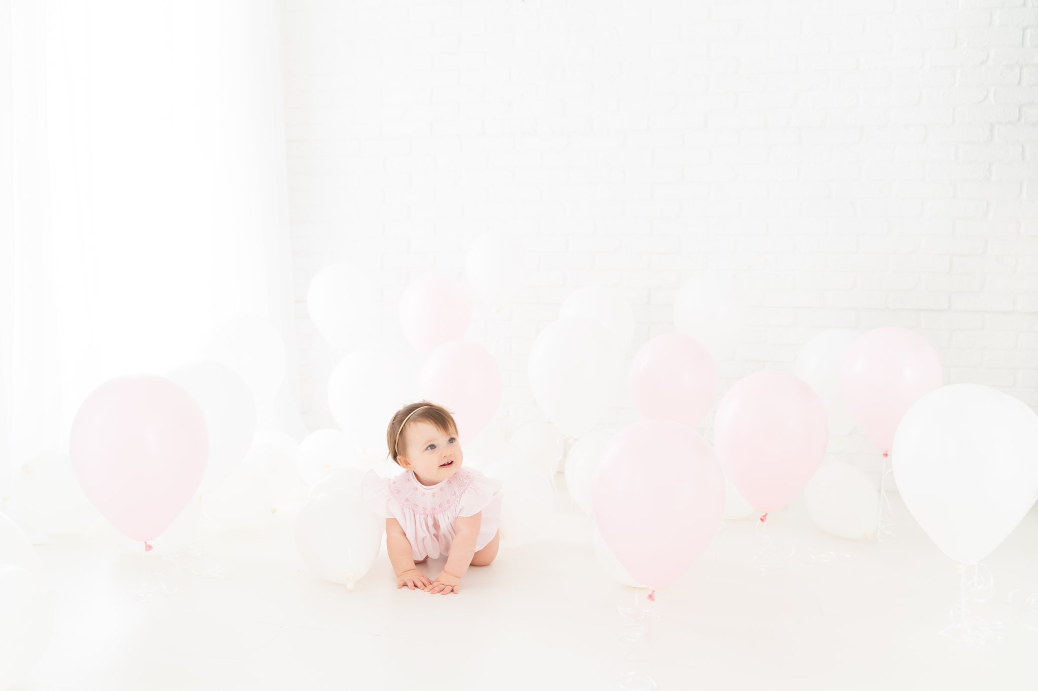 One Year old baby girl playing in a room full of balloons being  photographed in a jupiter florida photography studio.