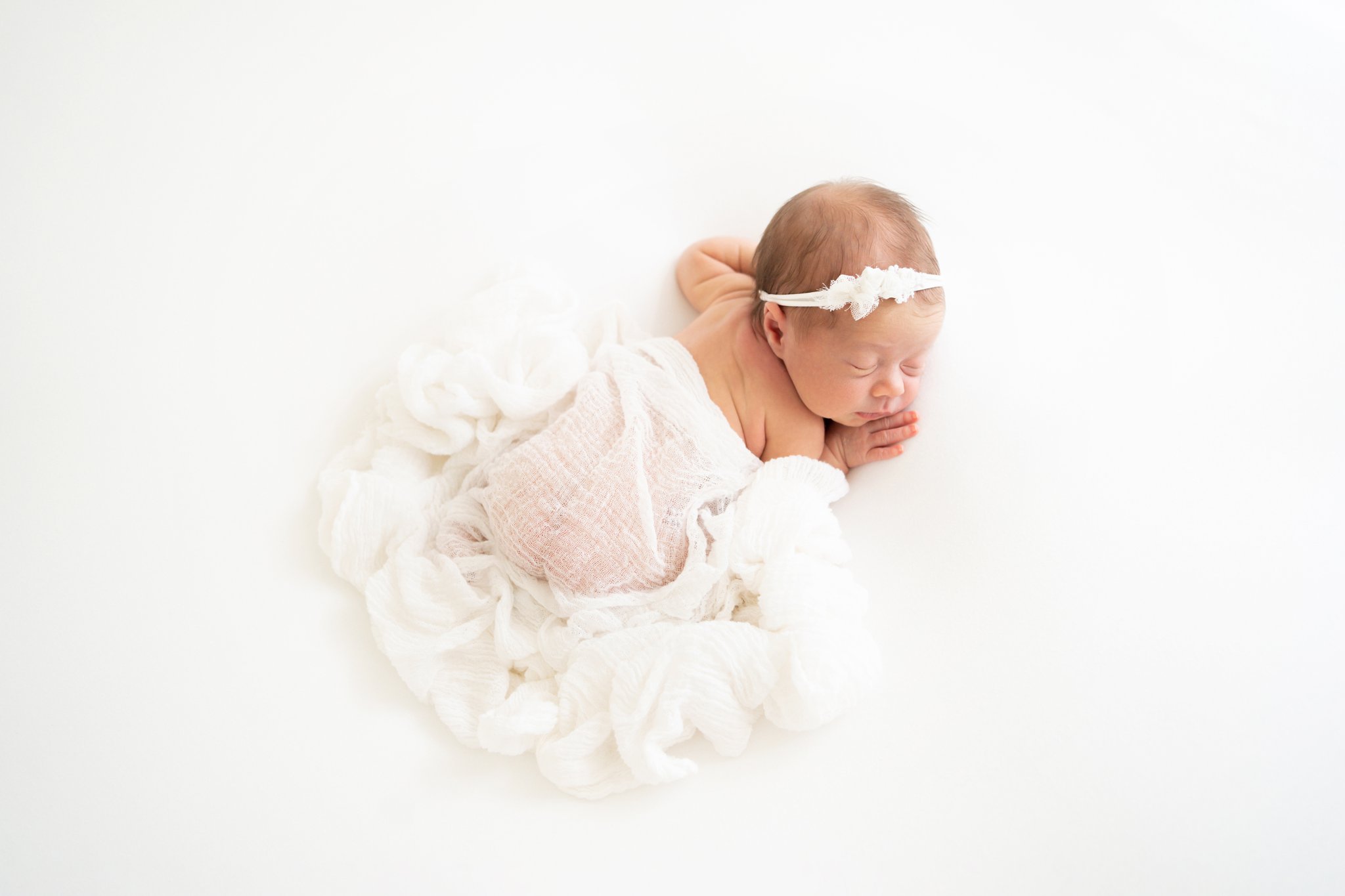 newborn baby laying on tummy covered in a white wrap being photographed in jupiter photography studio
