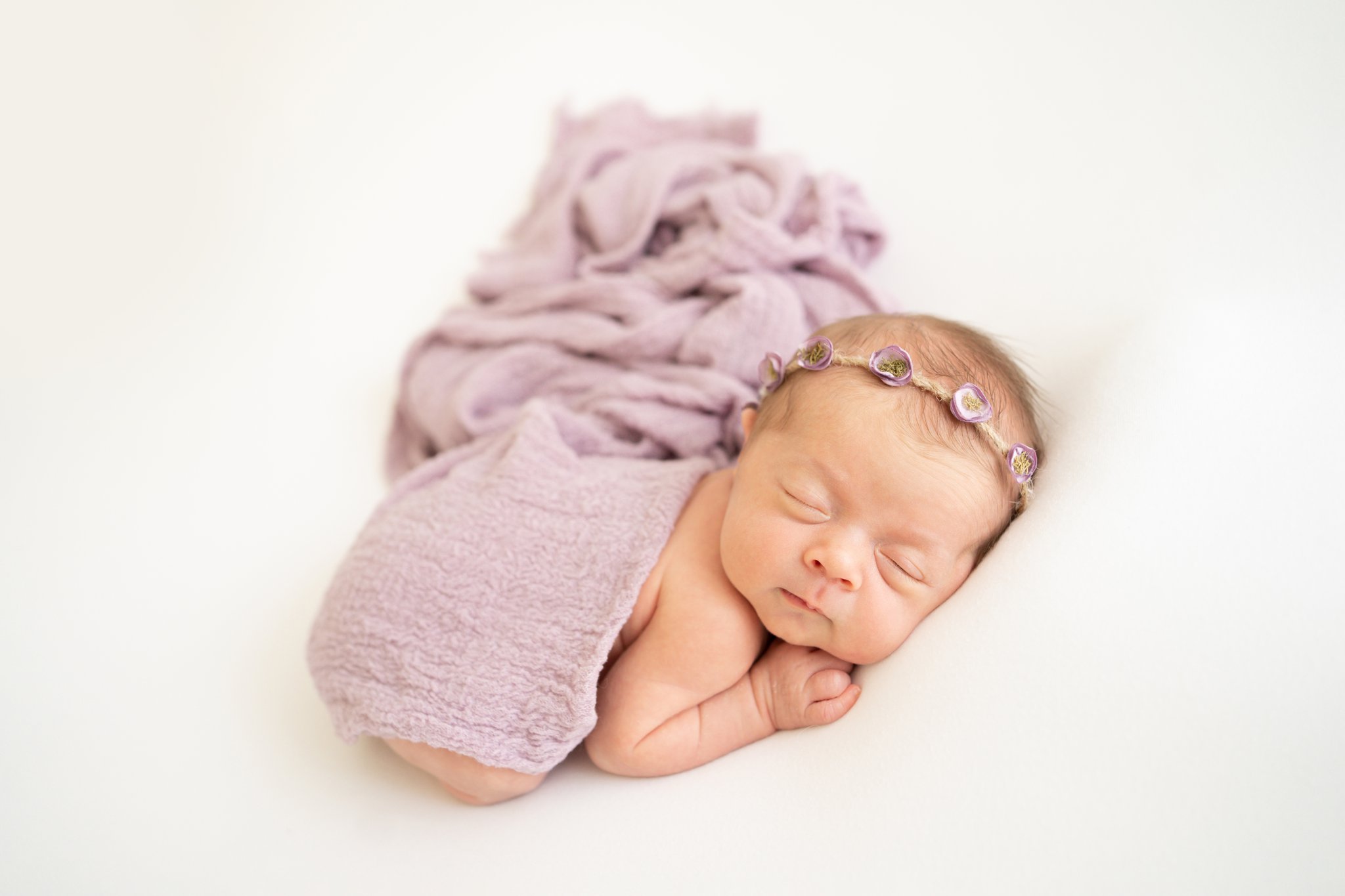 new baby laying on tummy with purple wrap being photographed in jupiter photography studio