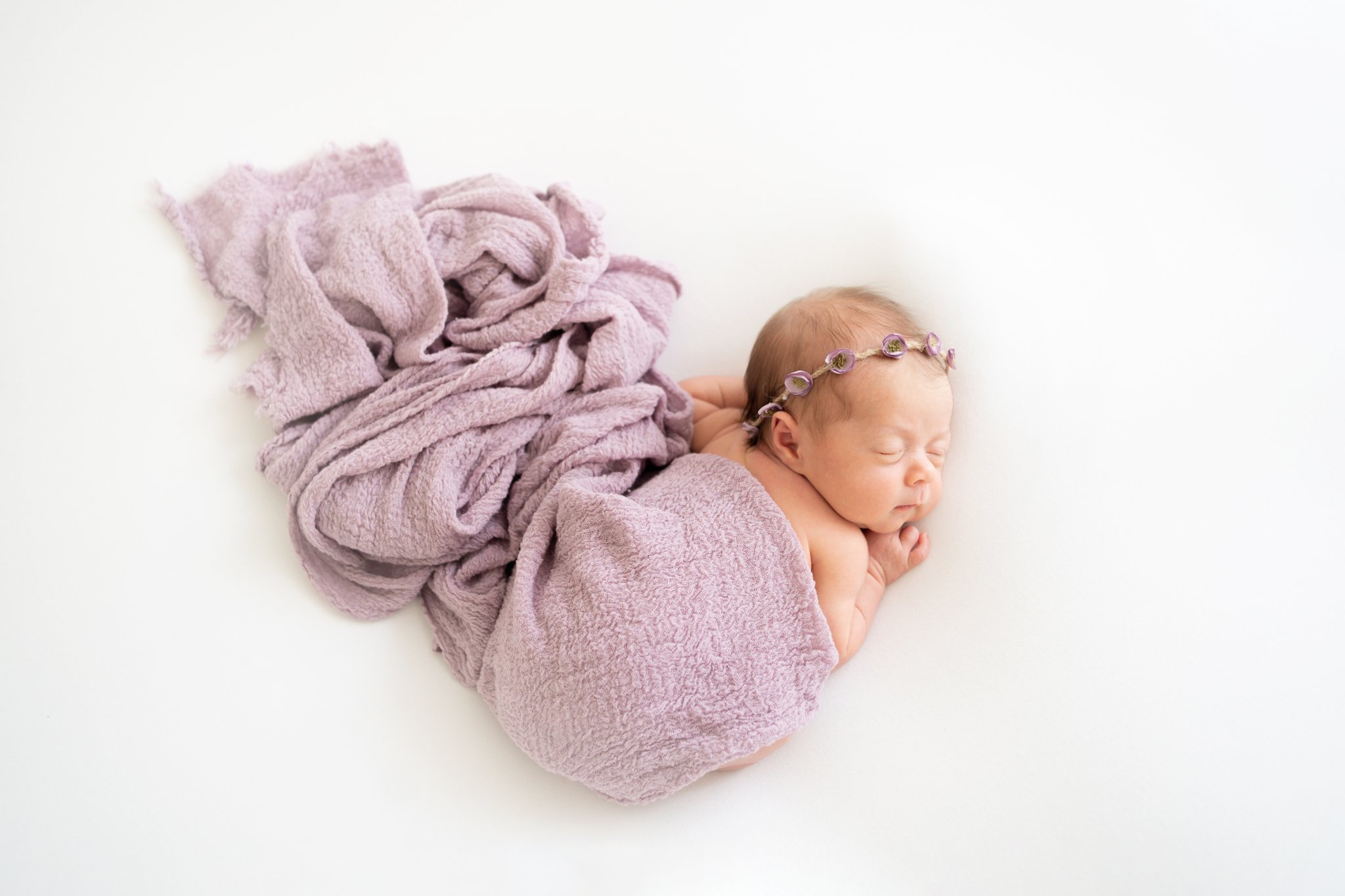Family Newborn Session  baby laying on tummy with purple wrap being photographed in jupiter photography studio
