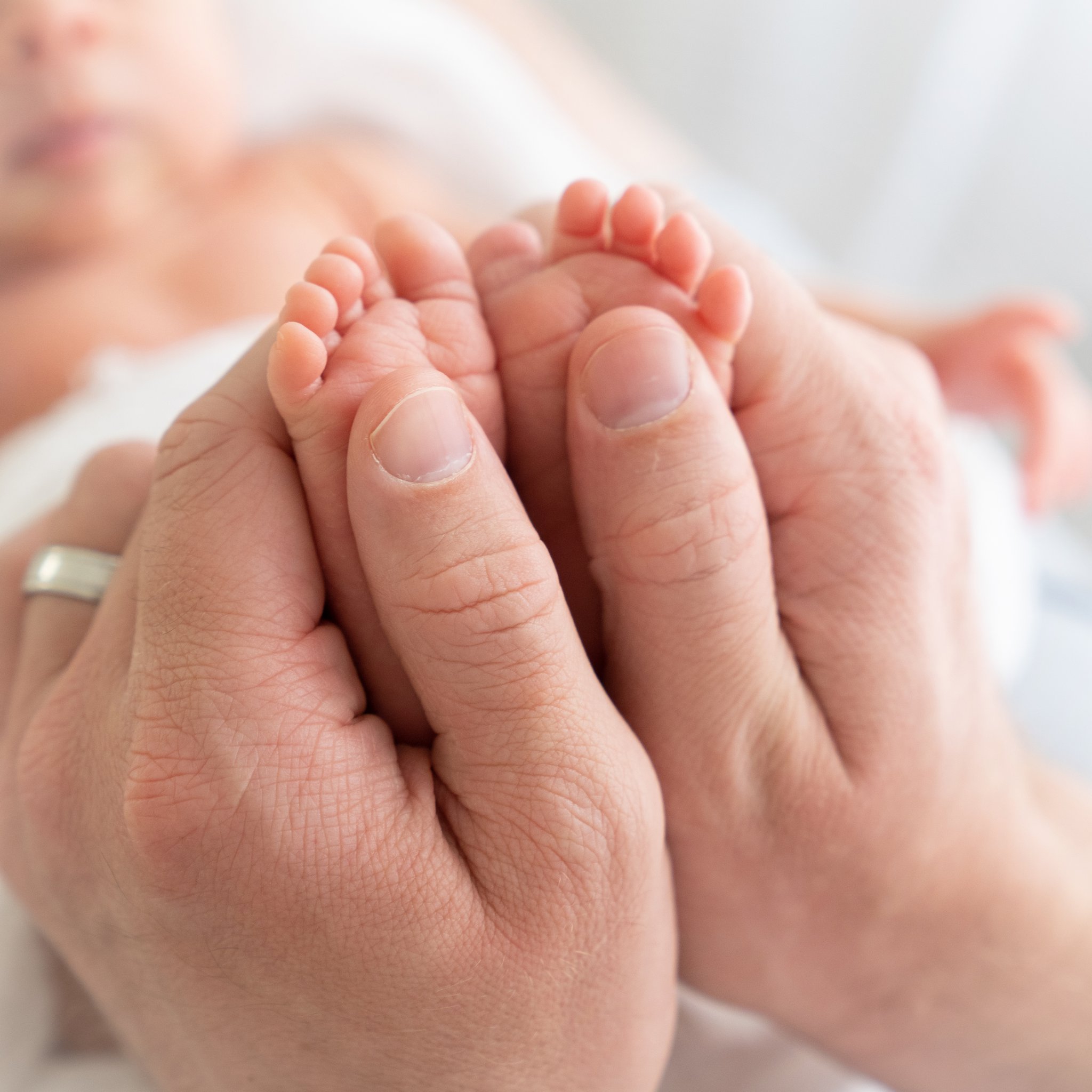 newborn baby's feet  and dad's thumbs close up being photographed in jupiter photography studio