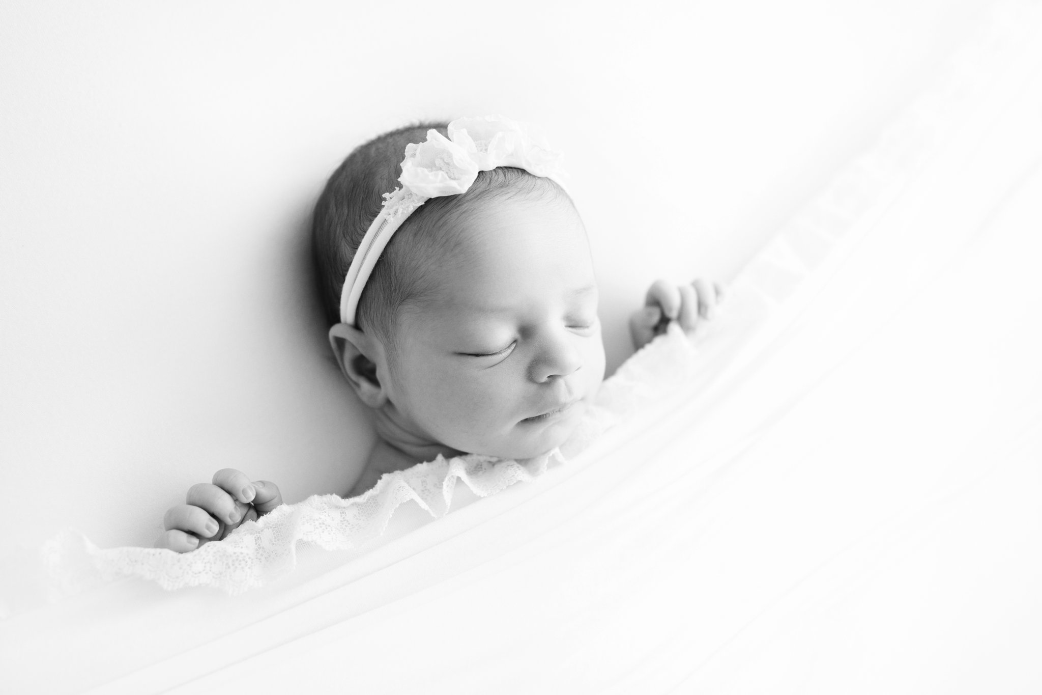 Black and white photo of a 2 weeek old baby laying on her back with a pretty headband 