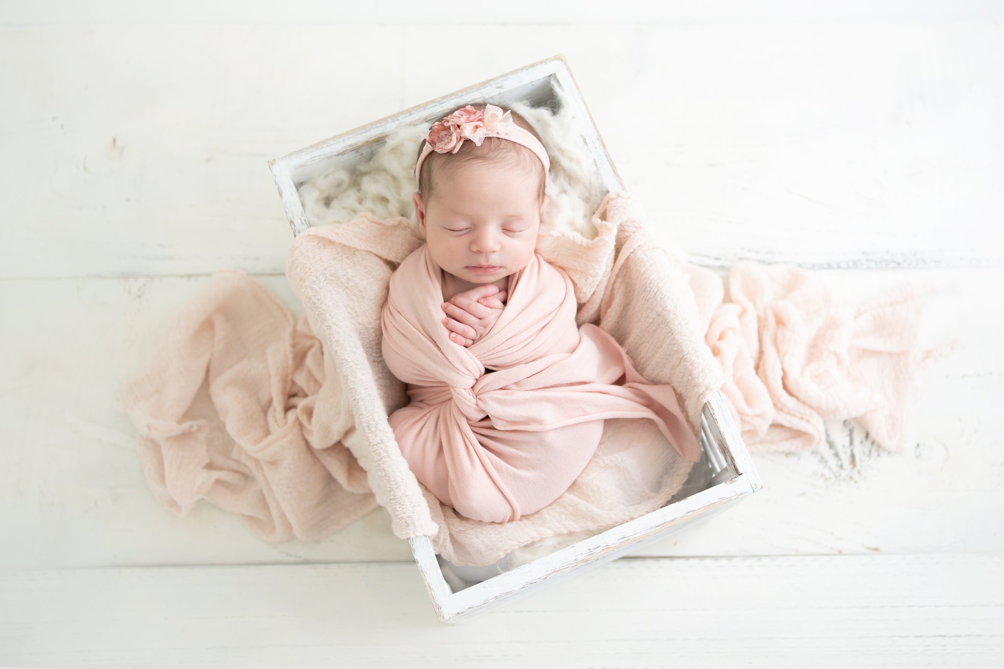 newborn baby baby being photographed in Jupiter baby photo studio laying in a wooden crate wrapped in pink