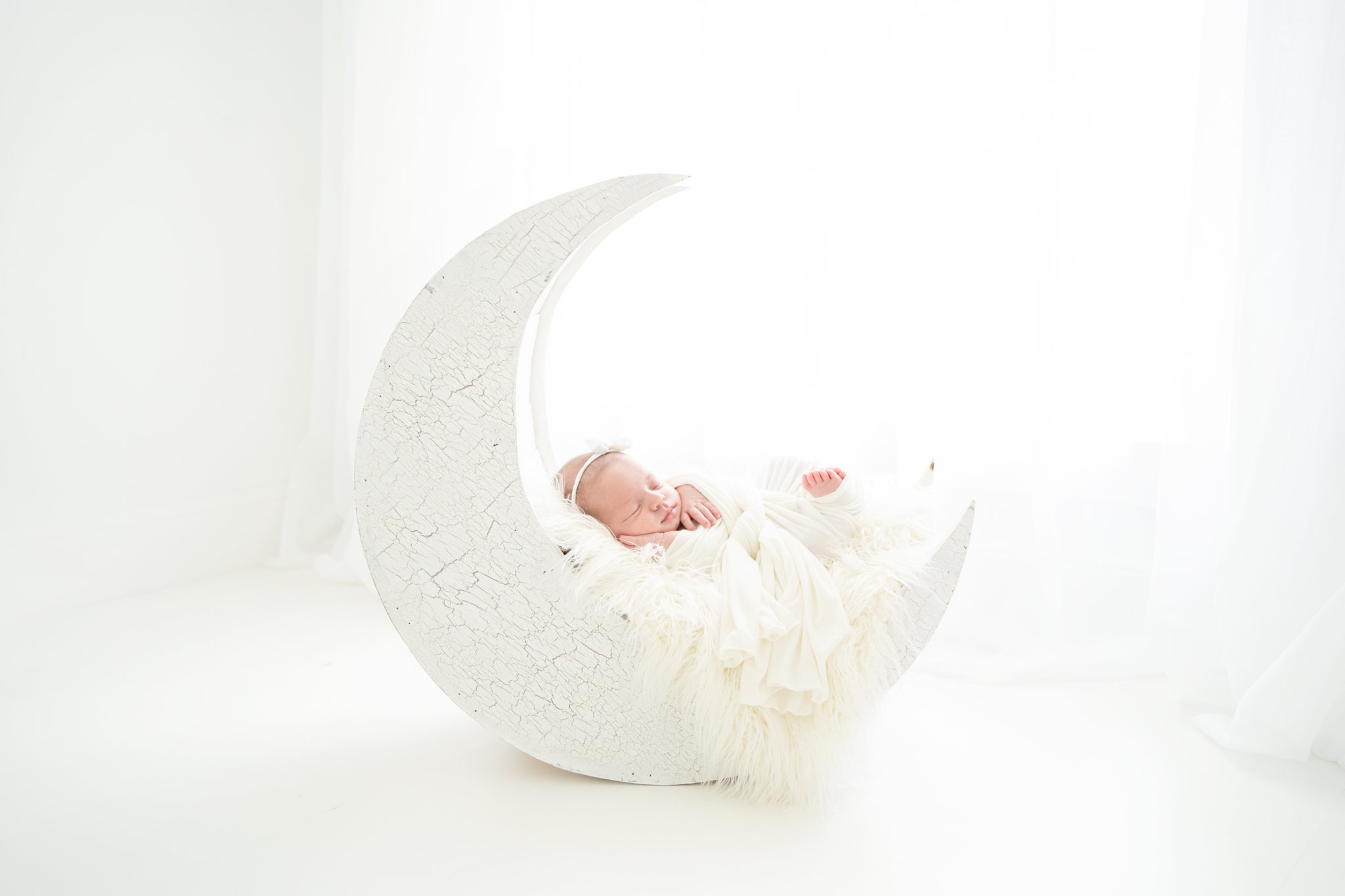 Newborn Photo Shoot featuring 2 week old baby girl wrapped in a white wrap laying in a moon prop