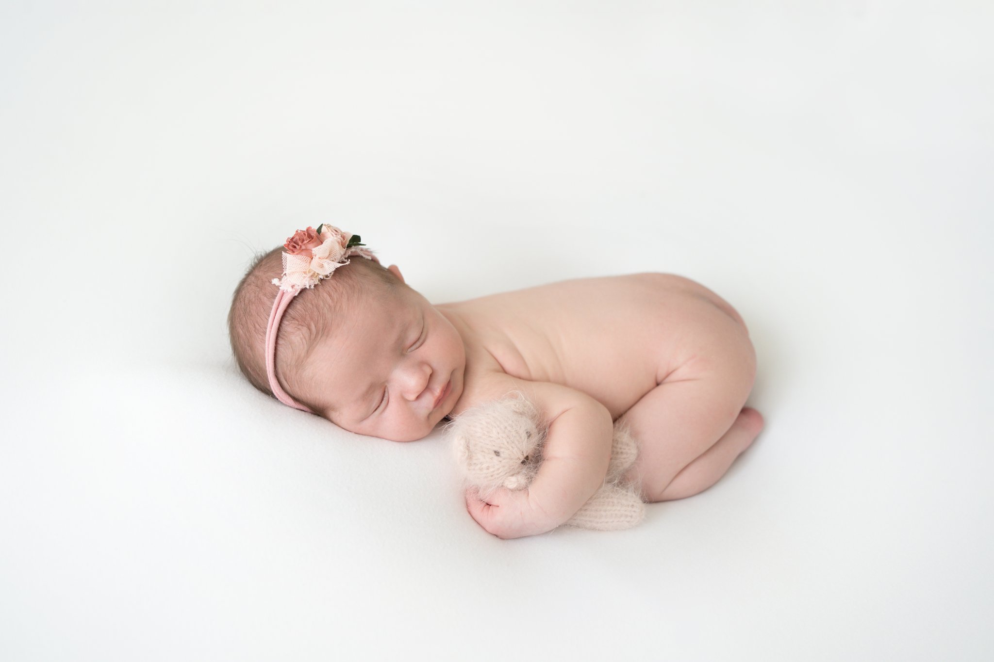 newborn baby baby being photographed in Jupiter baby photo studio laying down holding pink bear