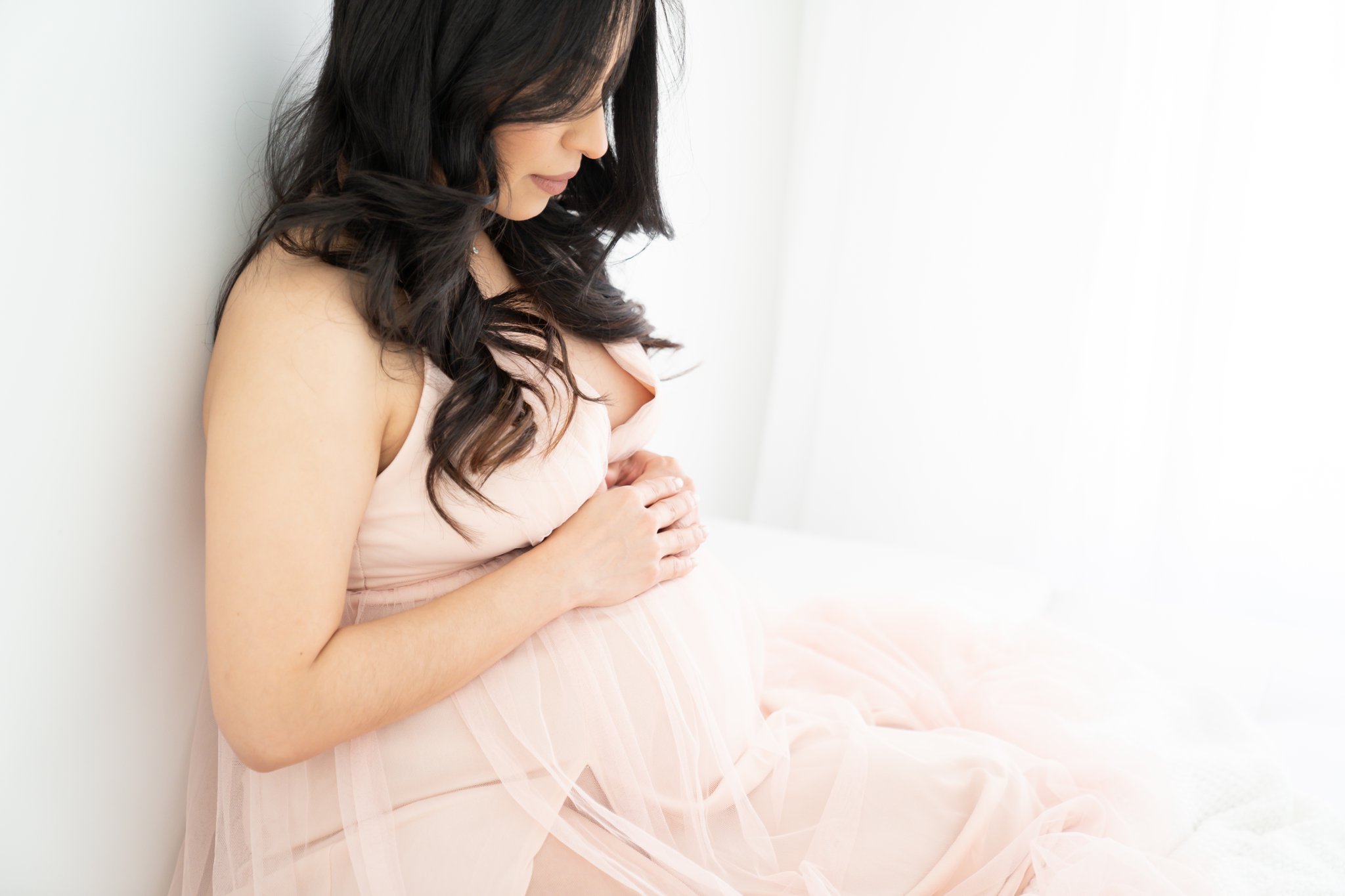 Pregnant mom being photographed in jupiter florida photography studio wearing a pink tulle maxi dress.
