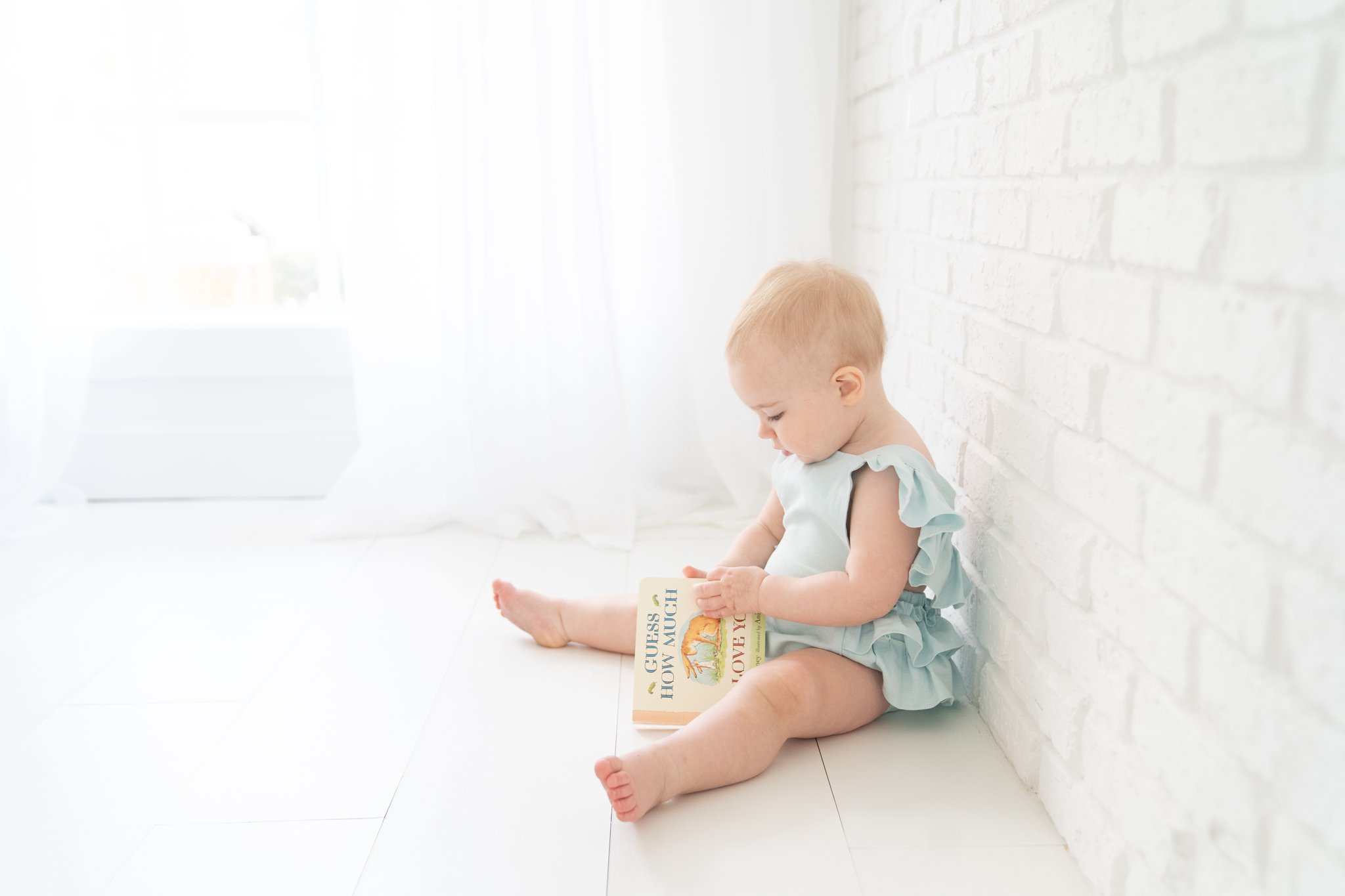  baby with blue romper reading Guess How Much I Love You book