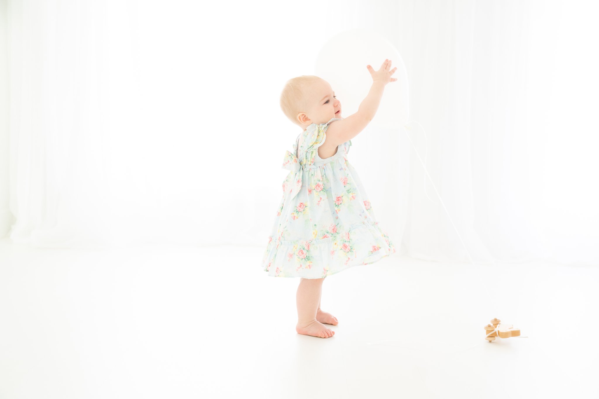 baby in a pretty blue dress playing with a single white birthday balloon
